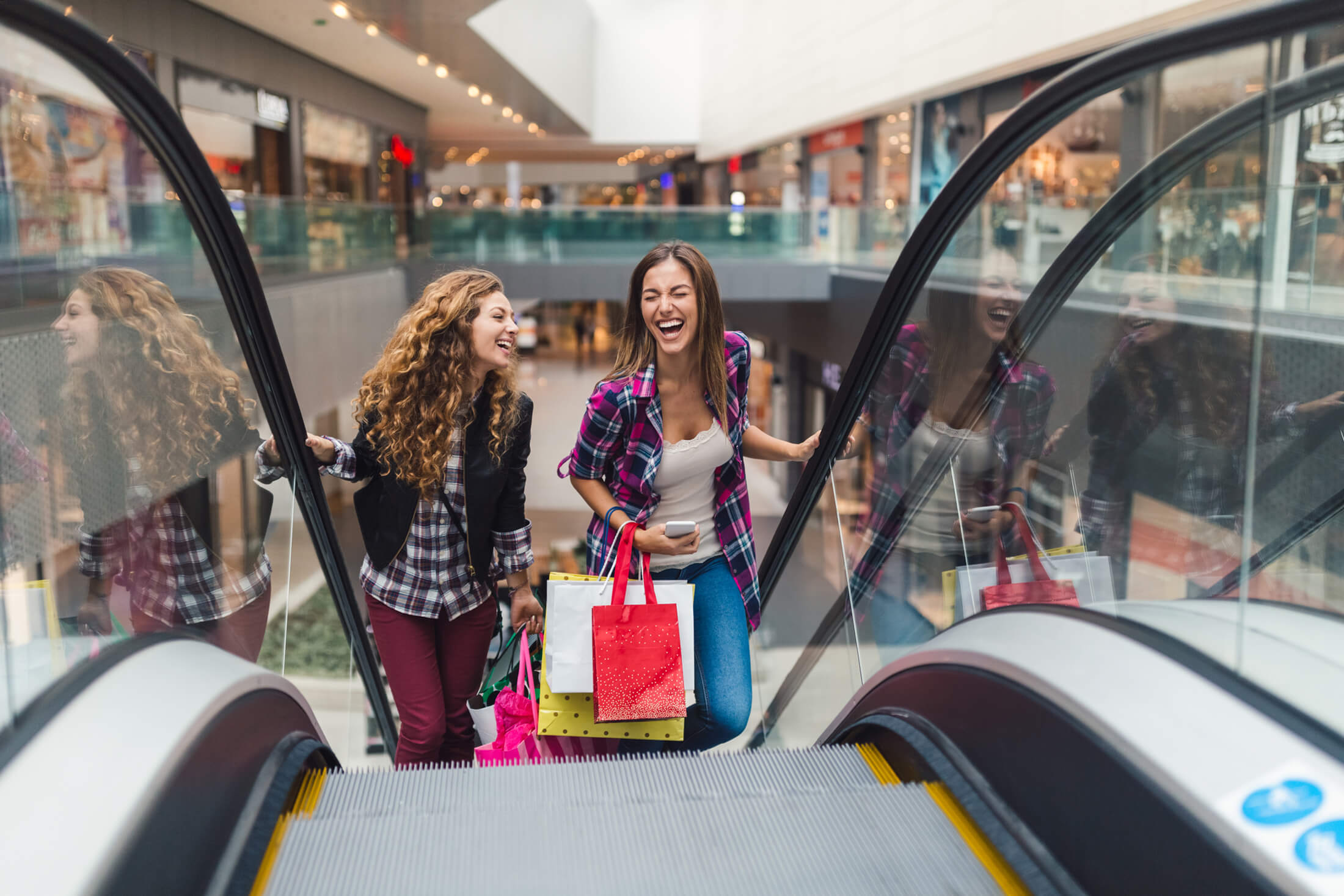 Two gals laughing on an escalator in a shopping mall